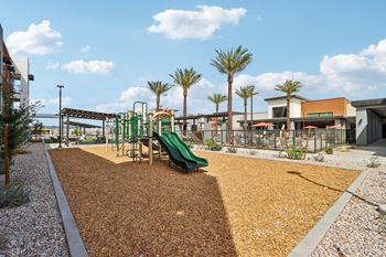 A playground with a green slide and brown mulch.